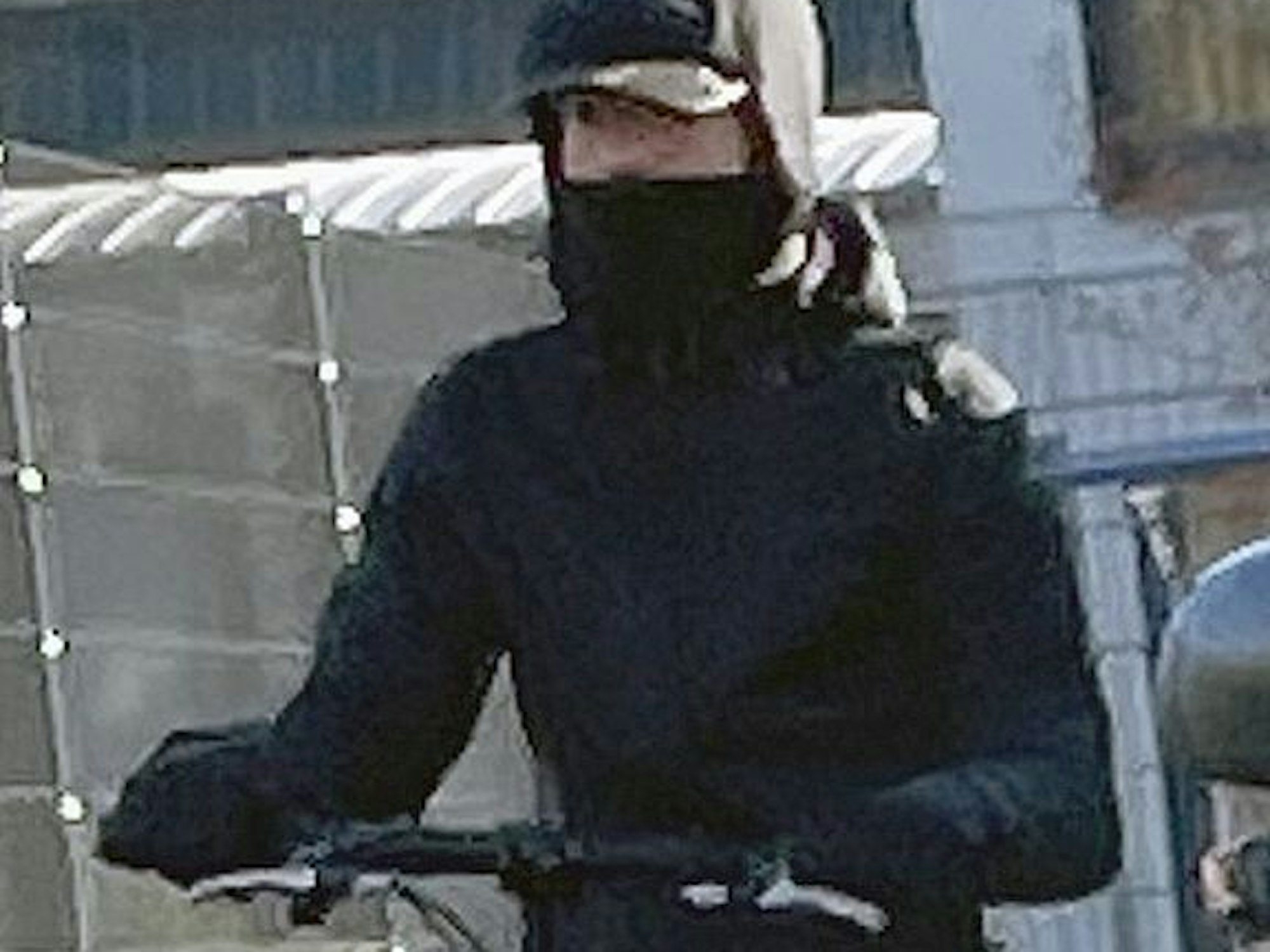 Eine Person mit Mütze und Tuch vor dem Mund steht auf einem E-Scooter.