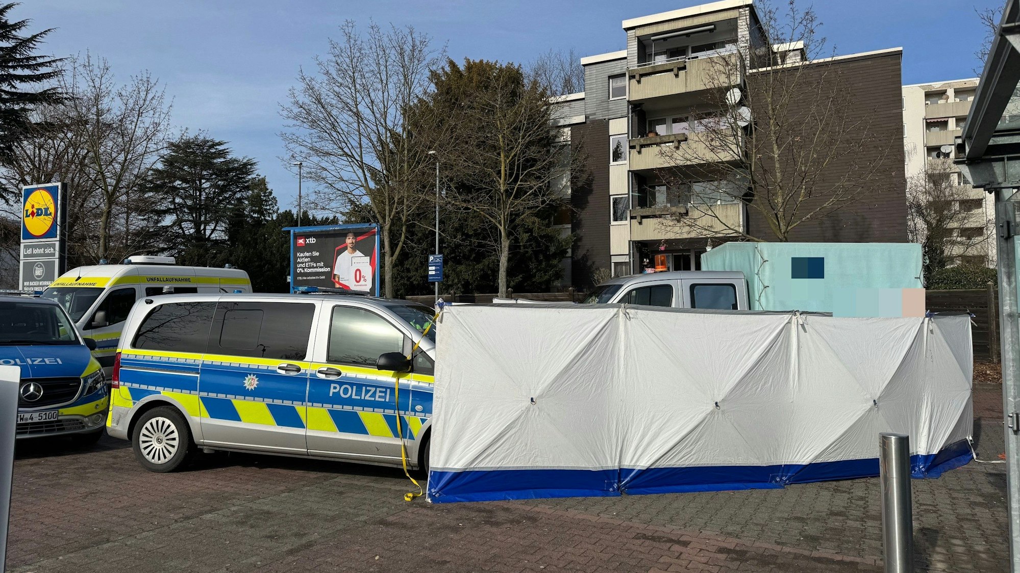 Ein Kleinlaster steht hinter einem Sichtschutz, daneben Einsatzfahrzeuge der Polizei.