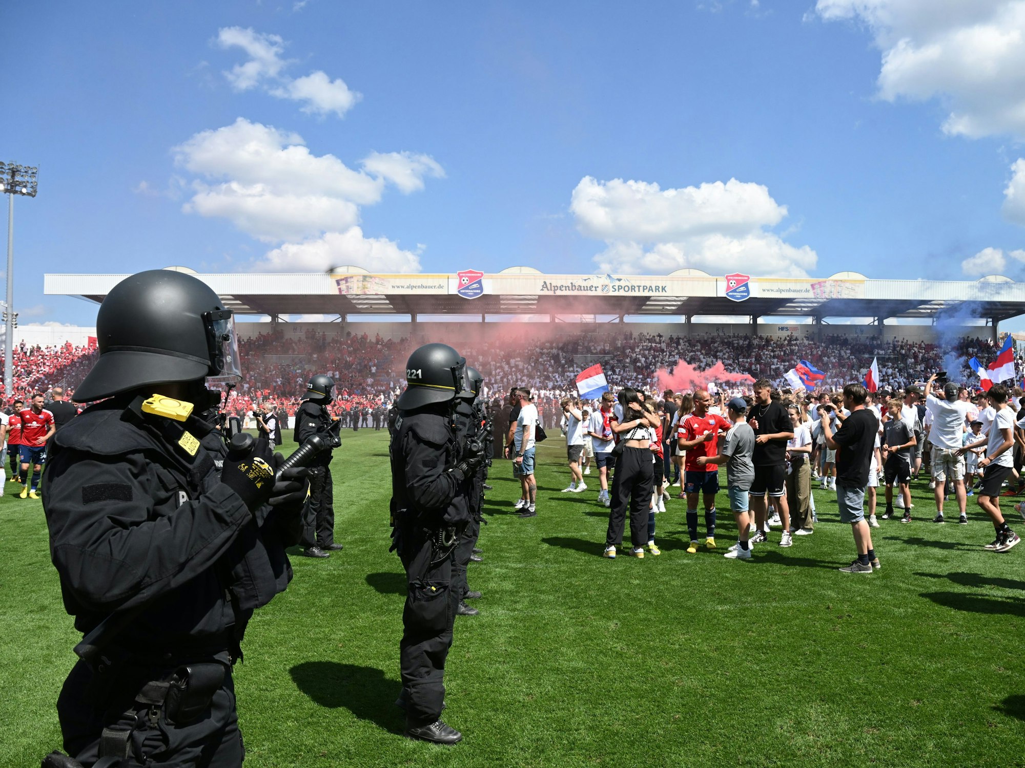 Fans stürmen den Rasen im Sportpark Unterhaching, im Vordergrund stehen Polizisten.