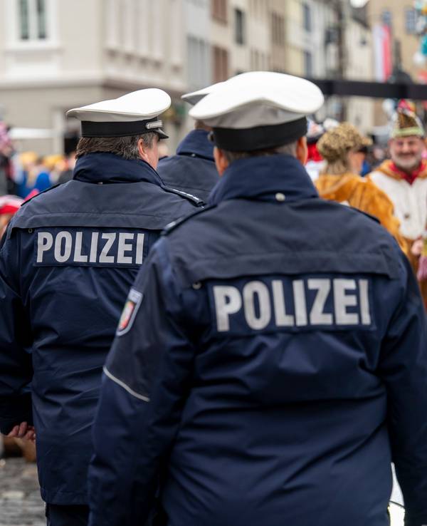 Polizisten laufen über eine Straße voller Karnevalisten.