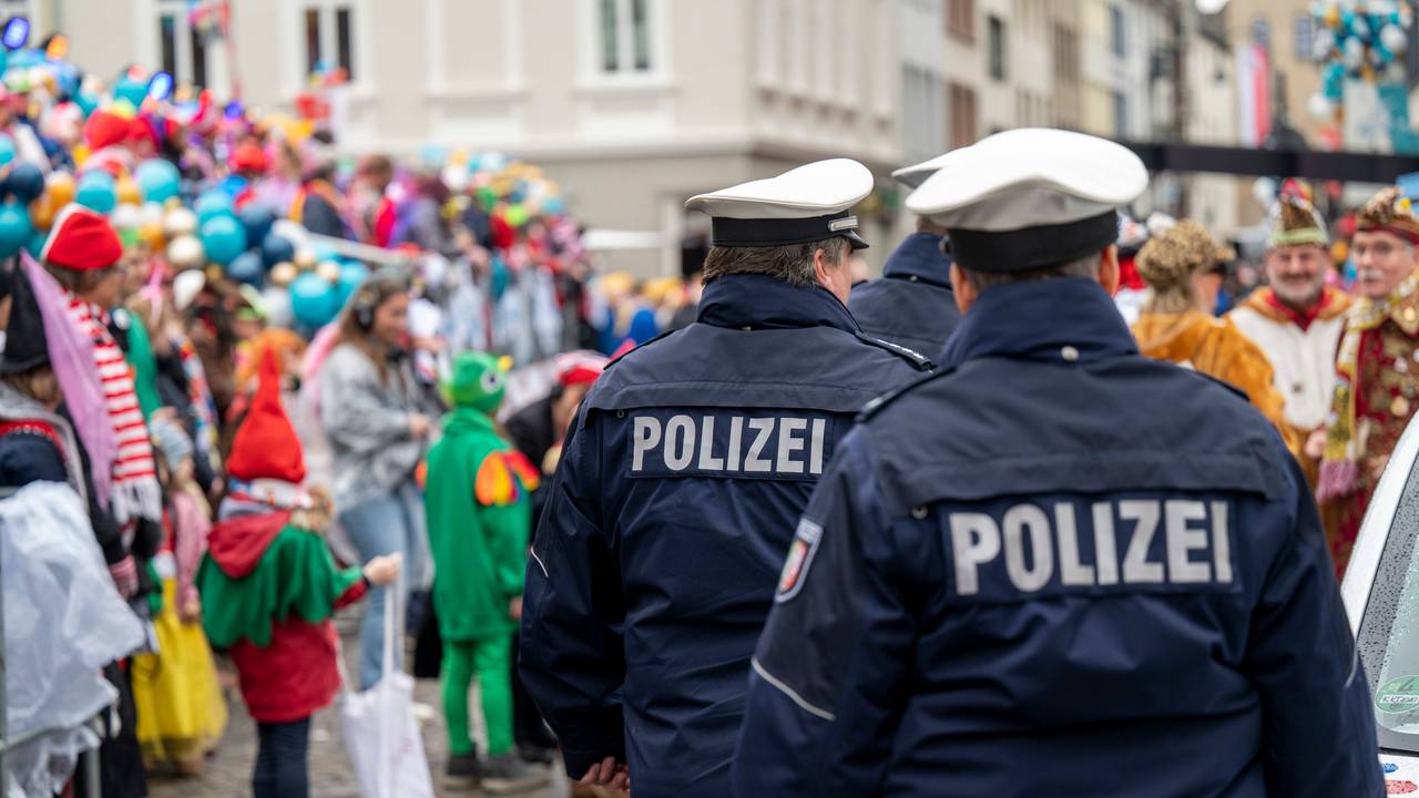 Polizisten laufen über eine Straße voller Karnevalisten.