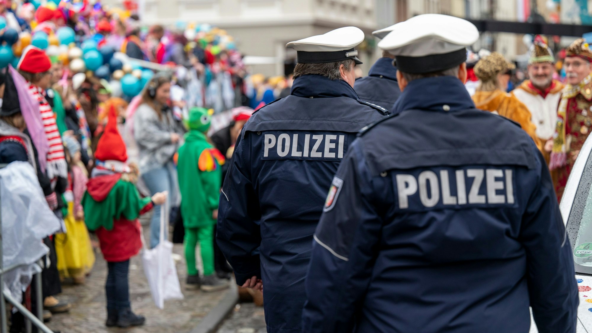 Polizisten laufen über eine Straße voller Karnevalisten.