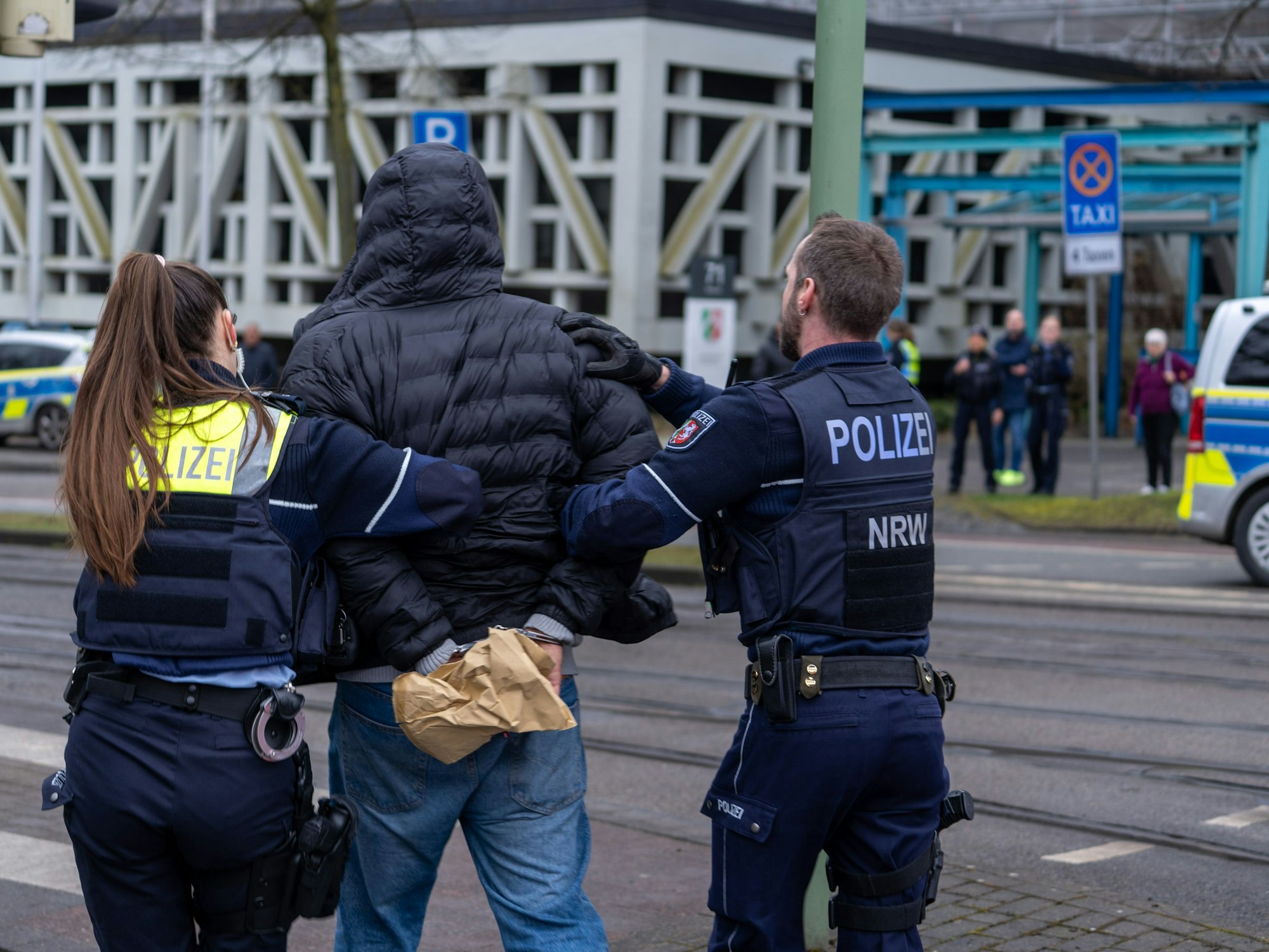 Einsatzkräfte der Polizei führen einen Mann in der Nähe von einem Tatort in Handschelllen ab.