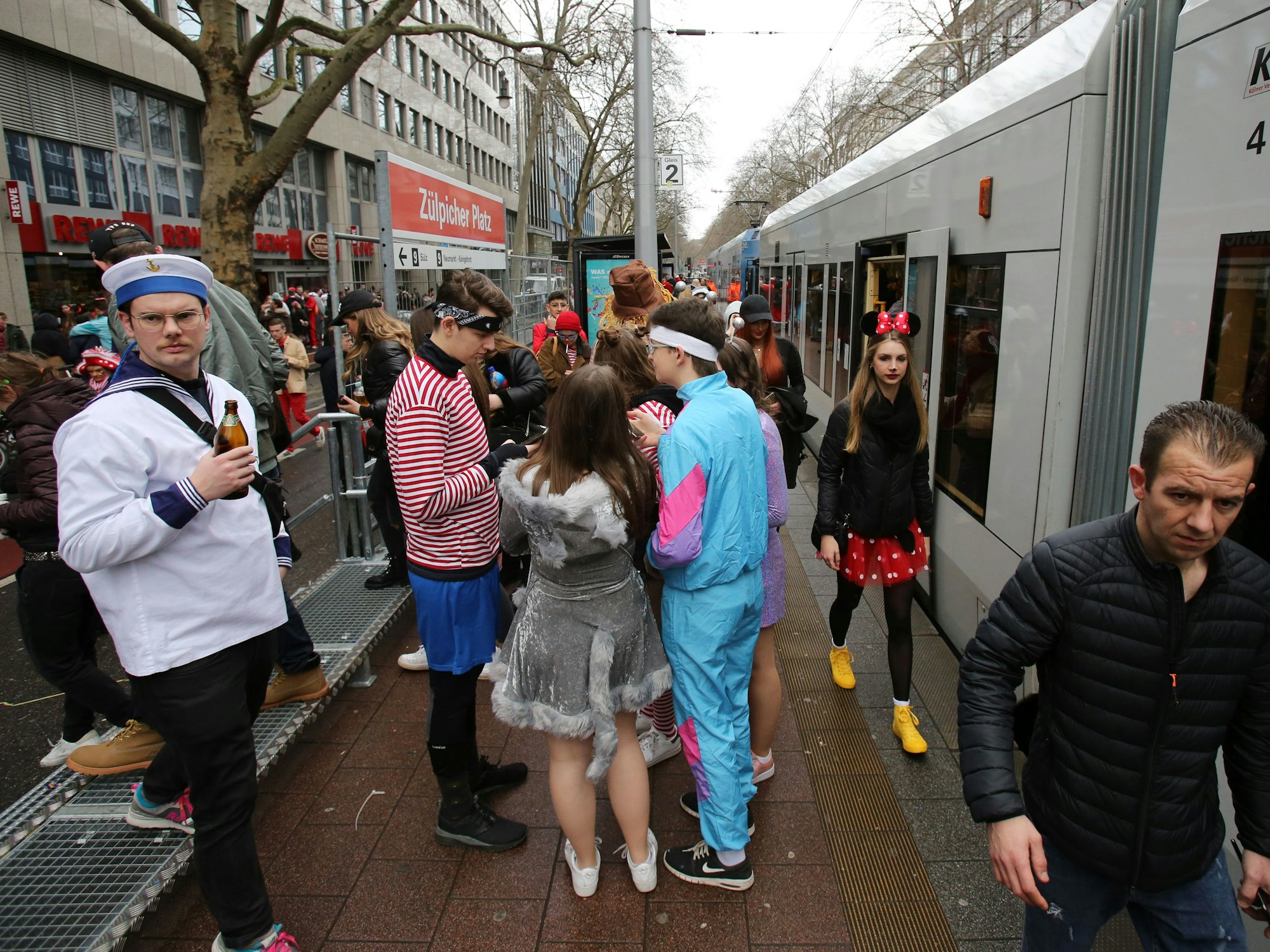 Menschen stehen verkleidet an einer KVB-Haltestelle in Köln.