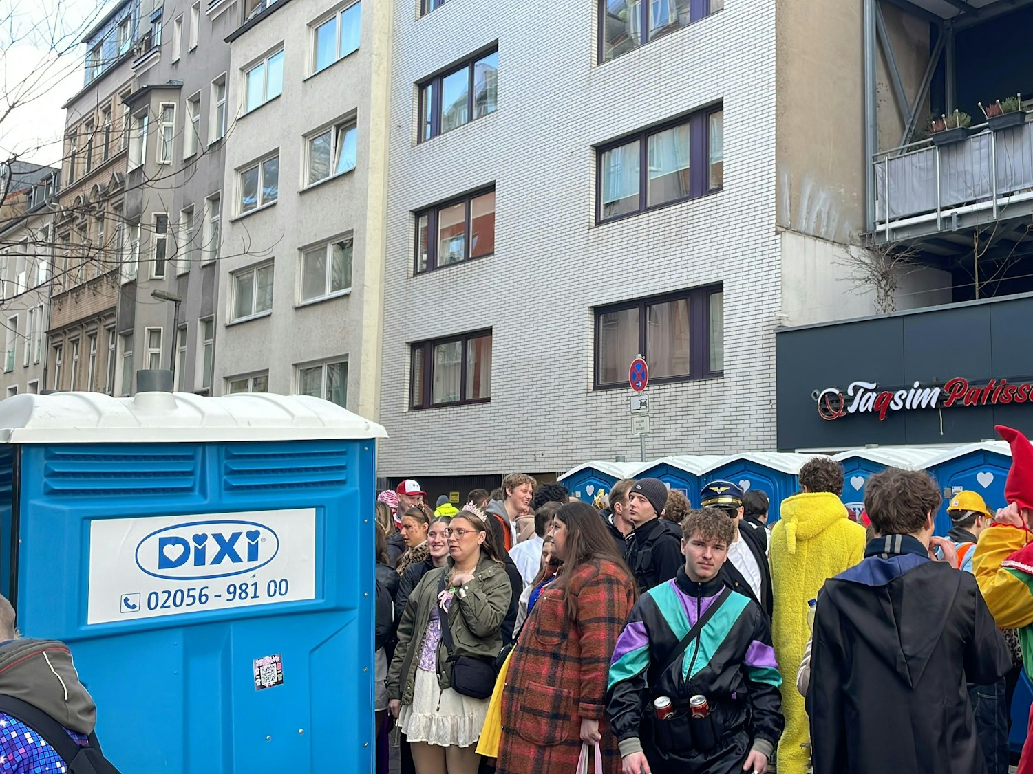 Menschen stehen an Karneval vor Dixi-Klos.