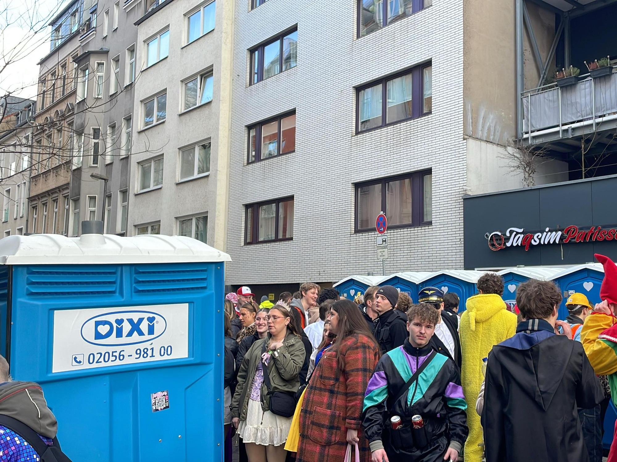 Menschen stehen an Karneval vor Dixi-Klos.