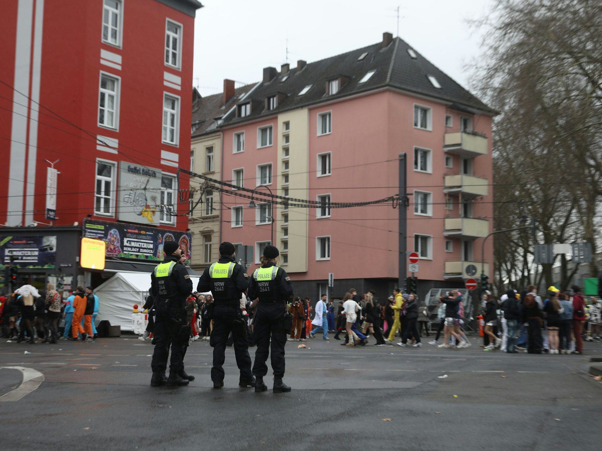 Einsatzkräfte der Polizei stehen an der Zülpicher Straße und verfolgen das Treiben an Weiberfastnacht in Köln.