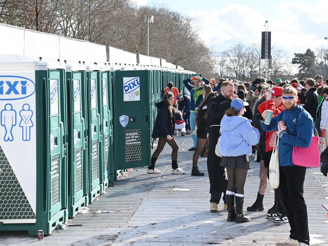Menschen stehen an Weiberfastnacht vor den mobilen Toiletten an der Uniwiese.