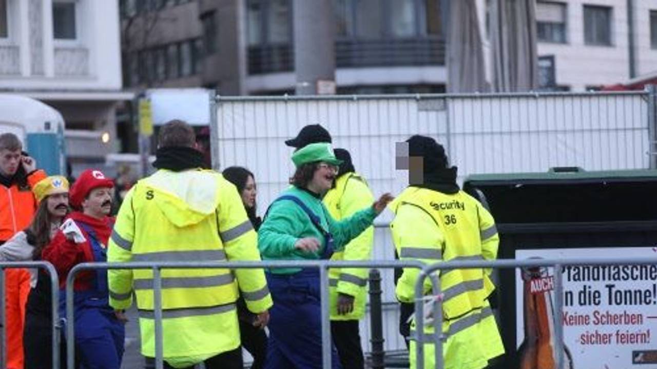Drei Sicherheitskräfte stehen an einer Absperrung und kontrollieren Feiernde.