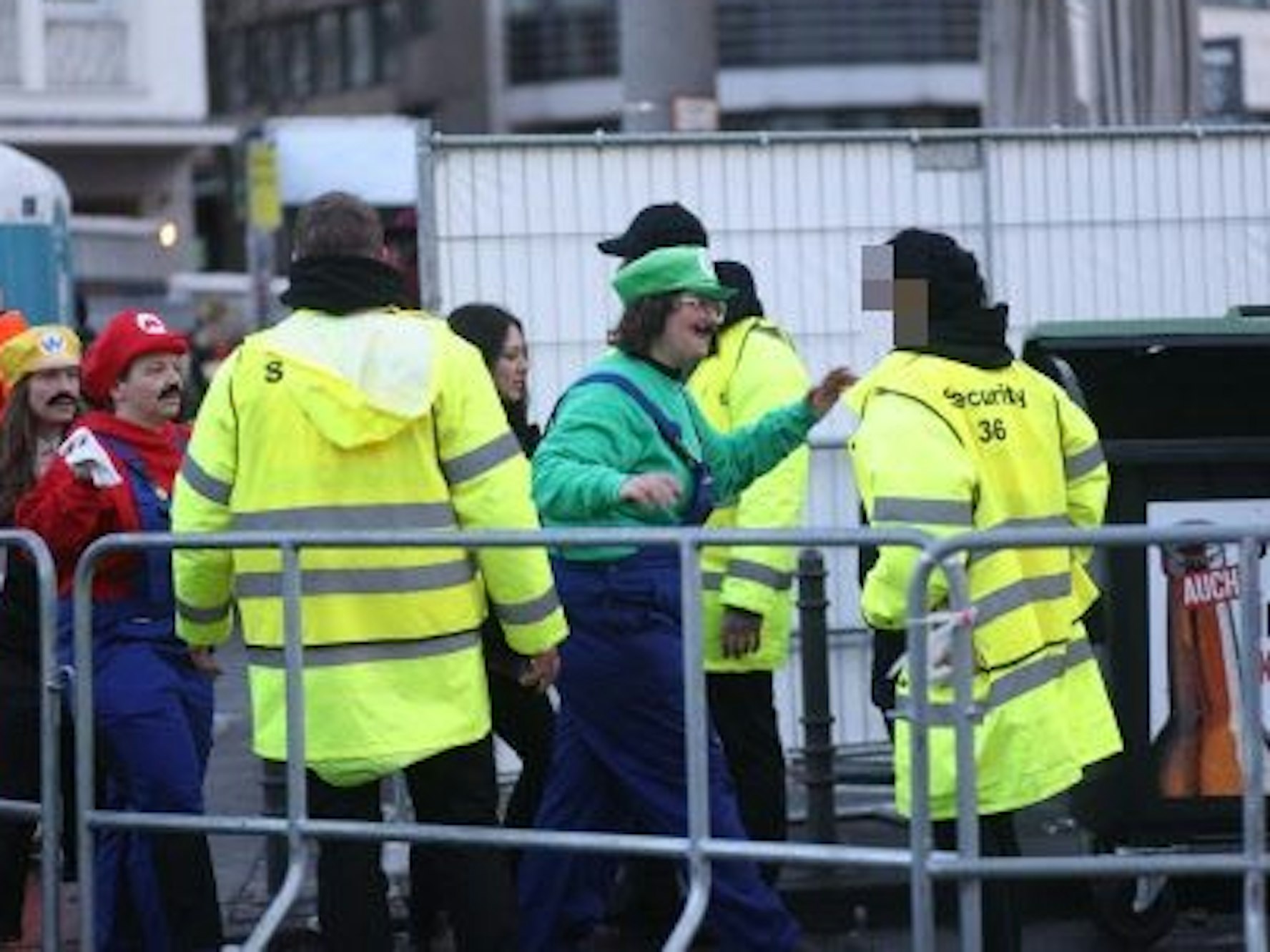 Drei Sicherheitskräfte stehen an einer Absperrung und kontrollieren Feiernde.