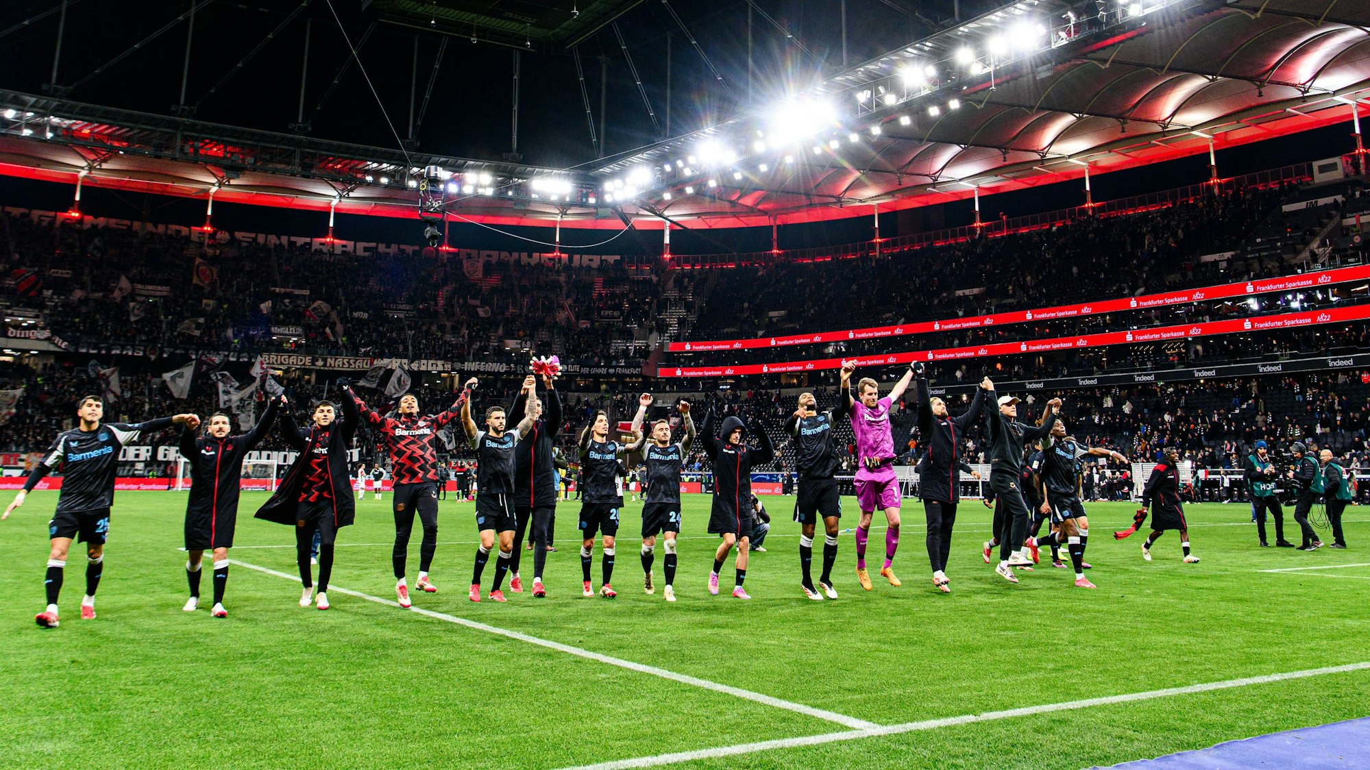 Während die Stars von Bayer Leverkusen mit ihren Fans den Sieg feiern, ist Jeremie Frimpong ganz rechts noch in der Nähe des dreiköpfigen TV-Teams zu sehen, mit dem er kurz zuvor gesprochen hat.