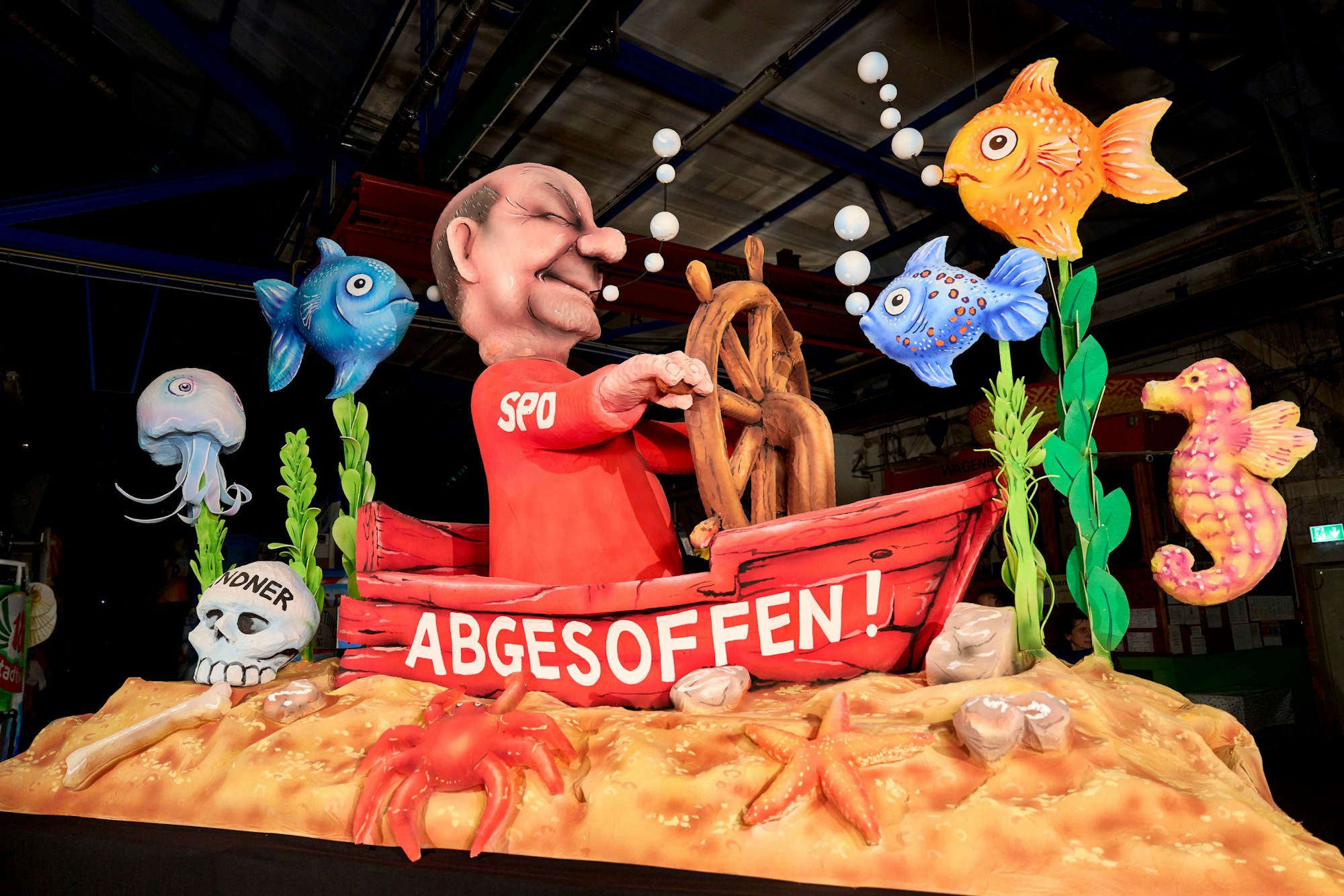Auf einem Mottowagen für den Rosenmontagszug ist Bundeskanzler Scholz am Steuer eines auf Grund gelaufenen Kahns stehend zu sehen.