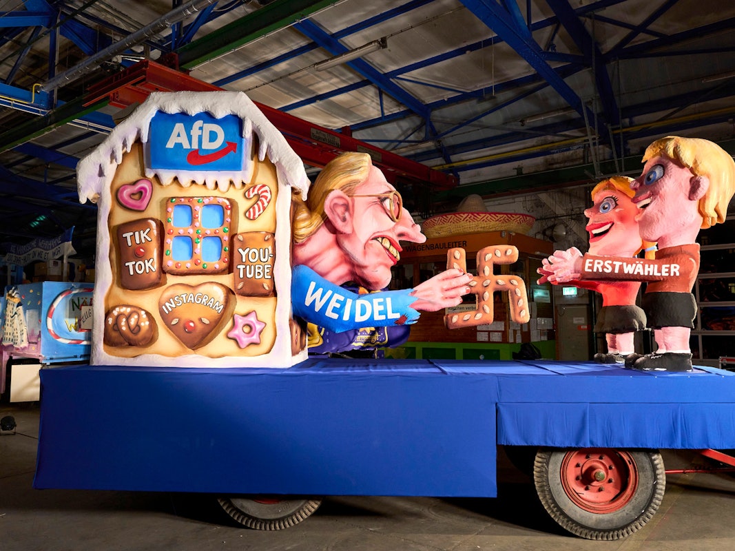 Auf einem Mottowagen für den Rosenmontagszug ist im Motiv des Märchens „Hänsel und Gretel“ AfD-Kanzlerkandidatin Alice Weidel zu sehen, die mit einem Lebkuchen-Hakenkreuz Erstwähler anlockt.