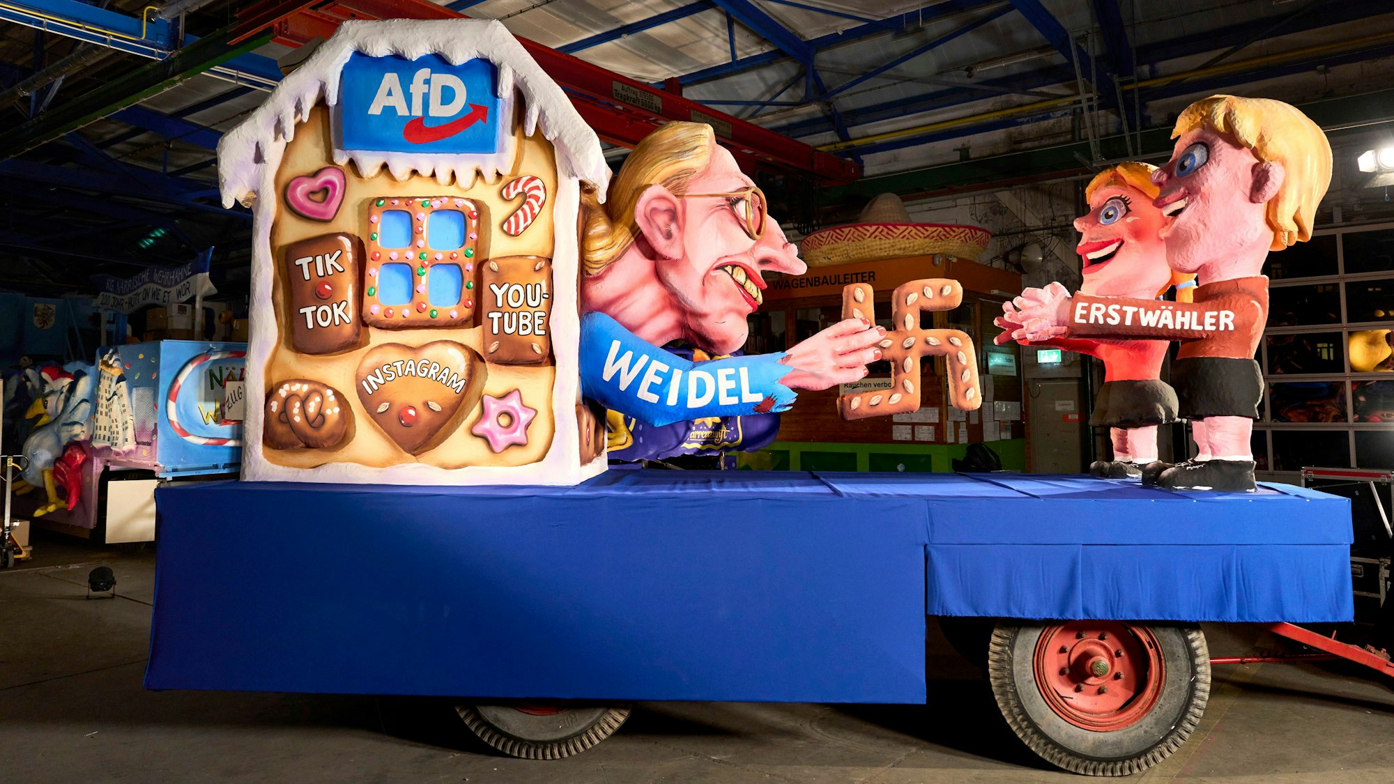 Auf einem Mottowagen für den Rosenmontagszug ist im Motiv des Märchens „Hänsel und Gretel“ AfD-Kanzlerkandidatin Alice Weidel zu sehen, die mit einem Lebkuchen-Hakenkreuz Erstwähler anlockt.
