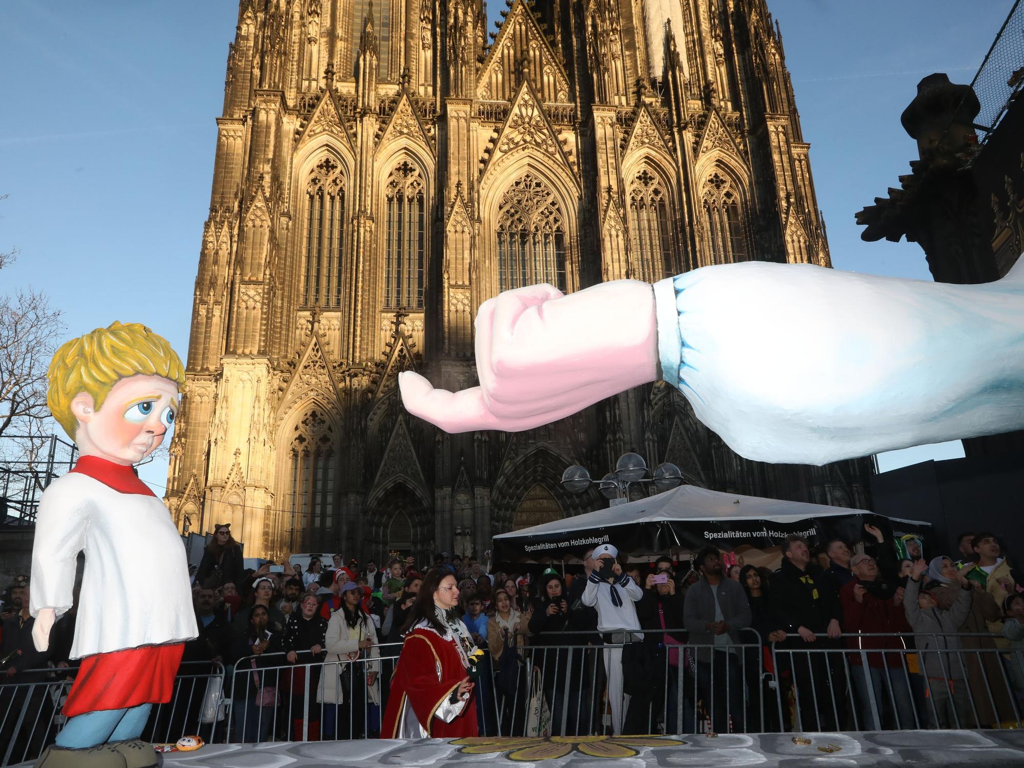 Auf einem Mottowagen, der am Kölner Dom vorbeifährt, lockt ein Finger einen kleinen Jungen.