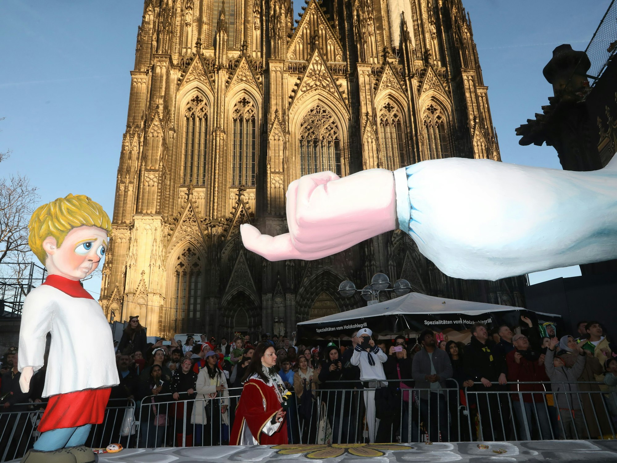 Auf einem Mottowagen, der am Kölner Dom vorbeifährt, lockt ein Finger einen kleinen Jungen.