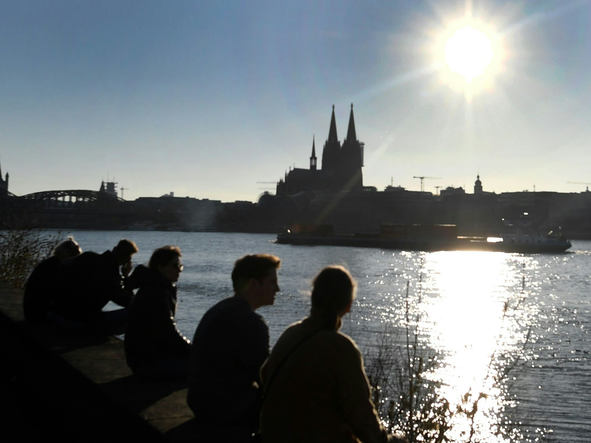 Das Wetter in Köln ist sonnig - und zwar schon Anfang März. Unser Symbolbild zeigt den Dom und den Rhein im Sonnenschein im Jahr 2021. Menschen genießen die Sonne vor dem Dom. +++ dpa-Bildfunk +++