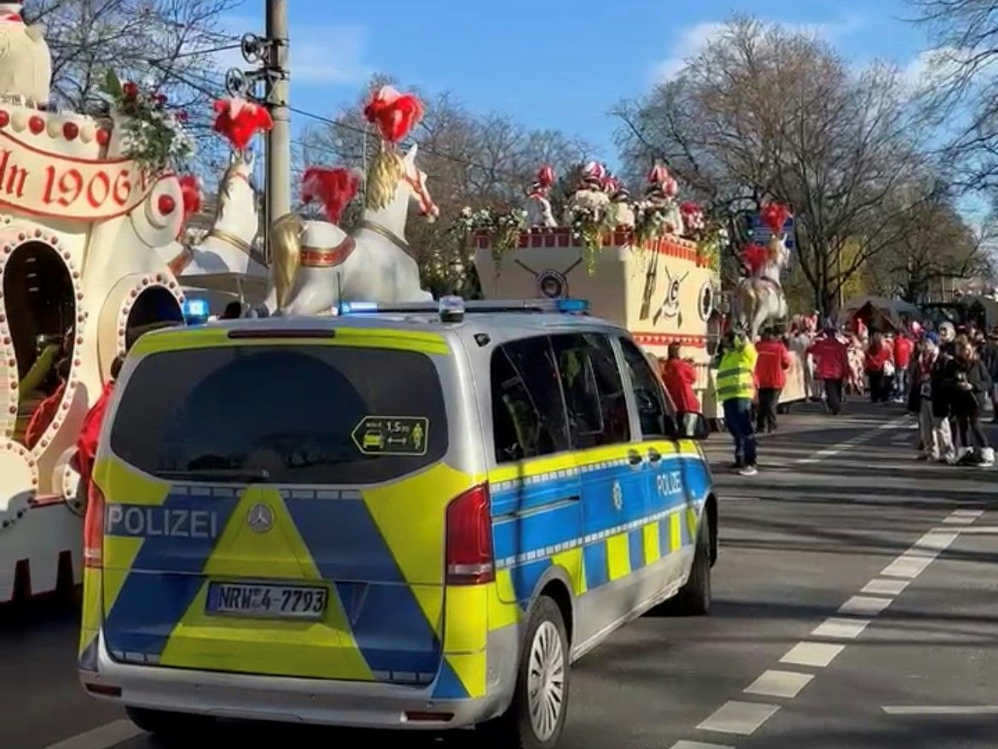 Karnevalswagen stehen auf einer Straße, daneben ein Polizeiwagen.