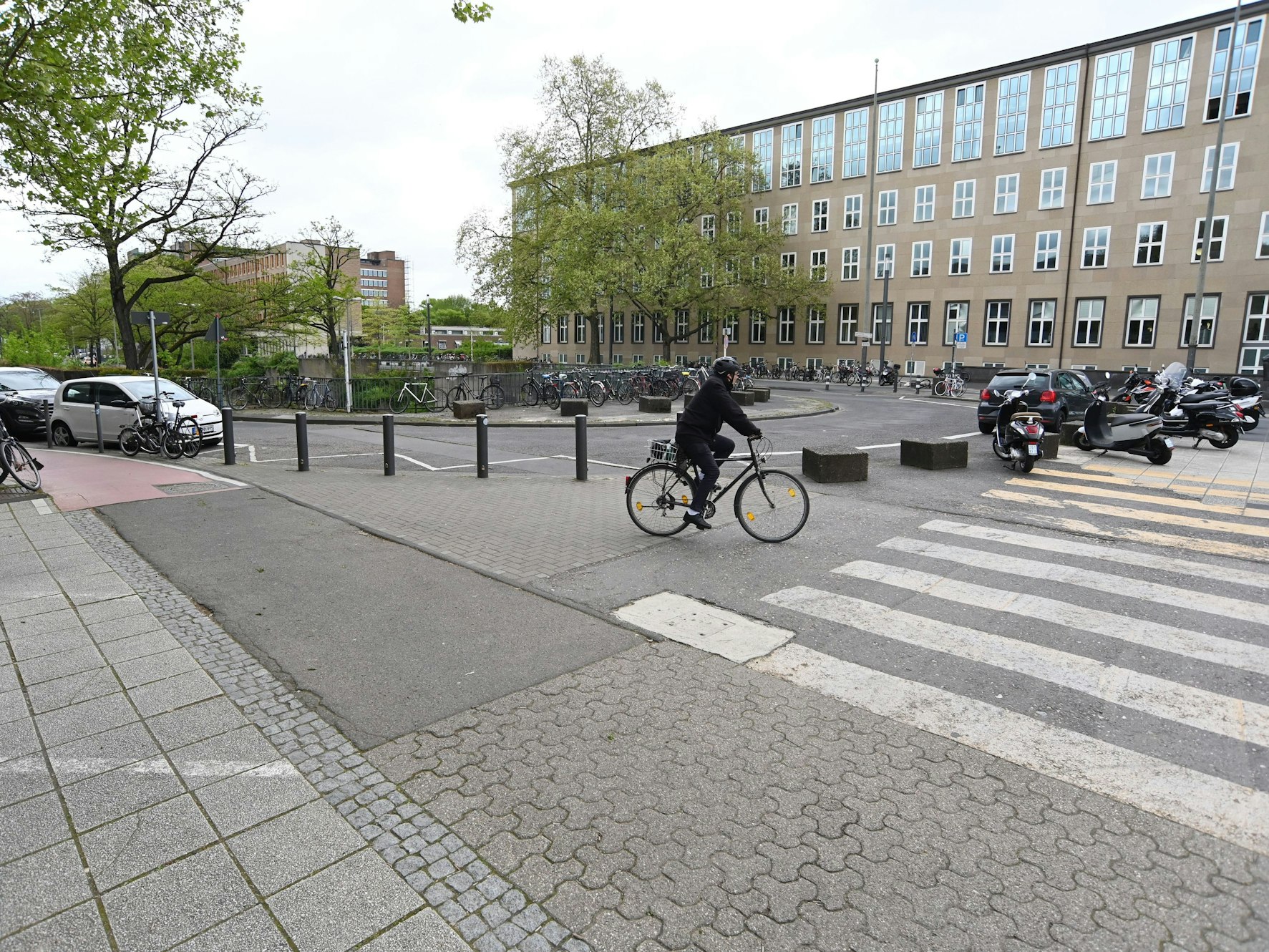 Ein Radfahrer und mehrere Autos stehen auf dem Albertus-Magnus-Platz vor der Universität zu Köln.