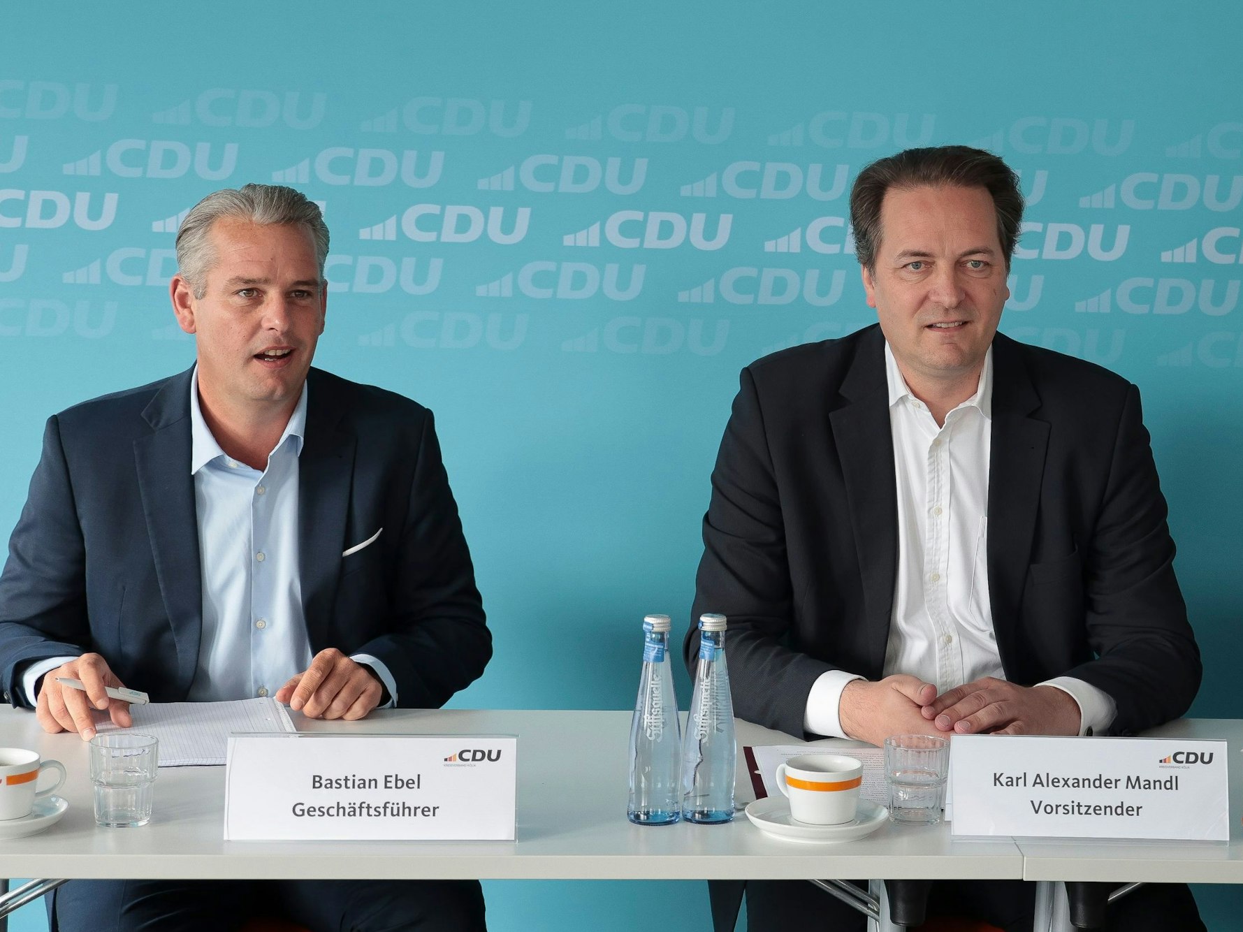 Bastian Ebel und Karl Alexander Mandl sitzen an einem Tisch bei einer Pressekonferenz.