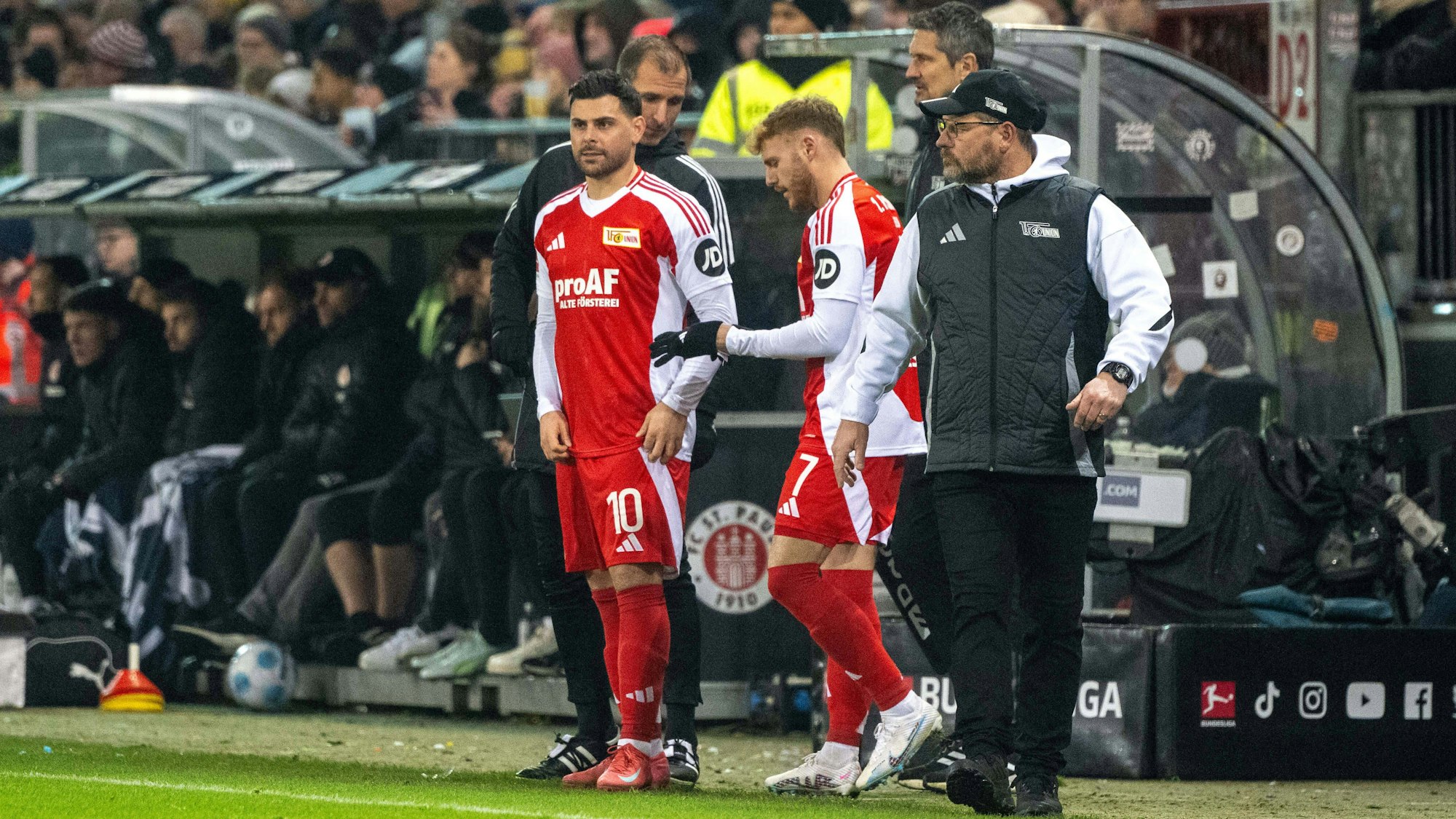 Kevin Volland (l.), Yorbe Vertessen (M.) und Trainer Steffen Baumgart stehen an der Seitenlinie.