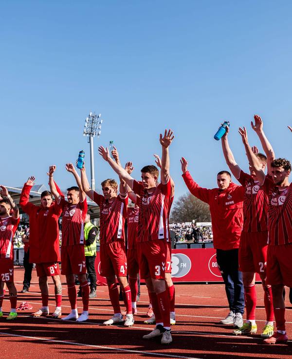 Die Spieler des 1. FC Köln stehen vor dem Auswärtsblock und heben die Arme in den Himmel.