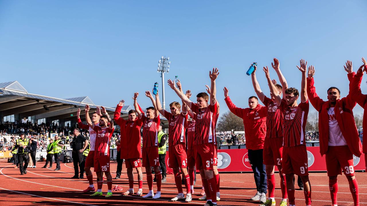Die Spieler des 1. FC Köln stehen vor dem Auswärtsblock und heben die Arme in den Himmel.