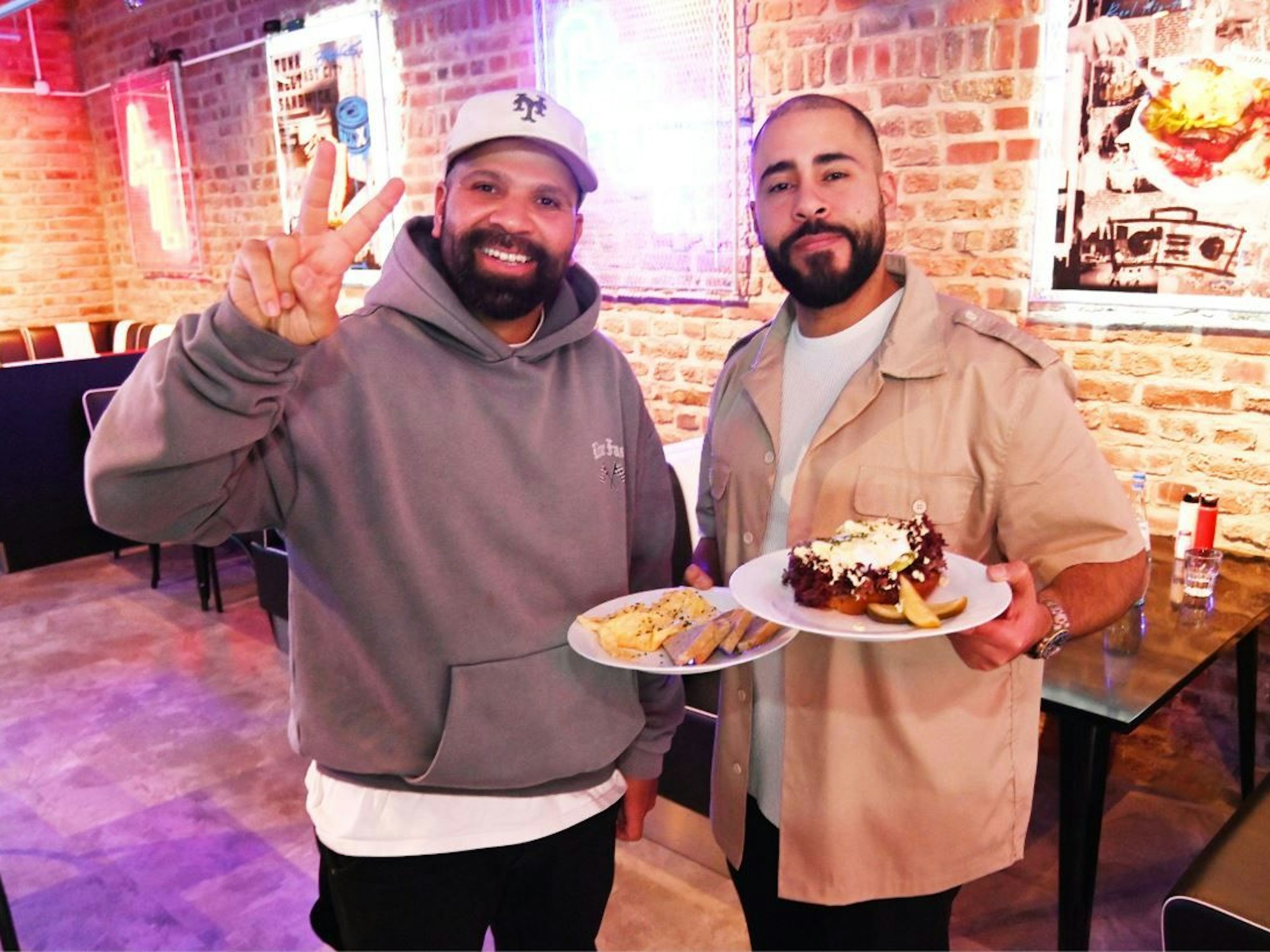 Zwei Männer stehen mit Frühstückstellern in einem Café.
