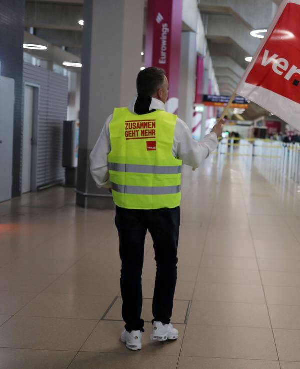 Mann mit Verdi-Fahne steht im Gebäude des Flughafens Köln/Bonn und streikt.