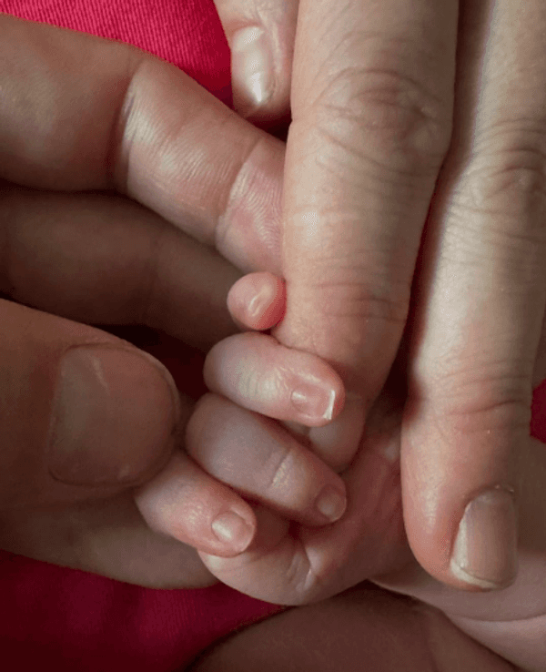 Eine Baby-Hand zwischen Fingern von Erwachsenen.