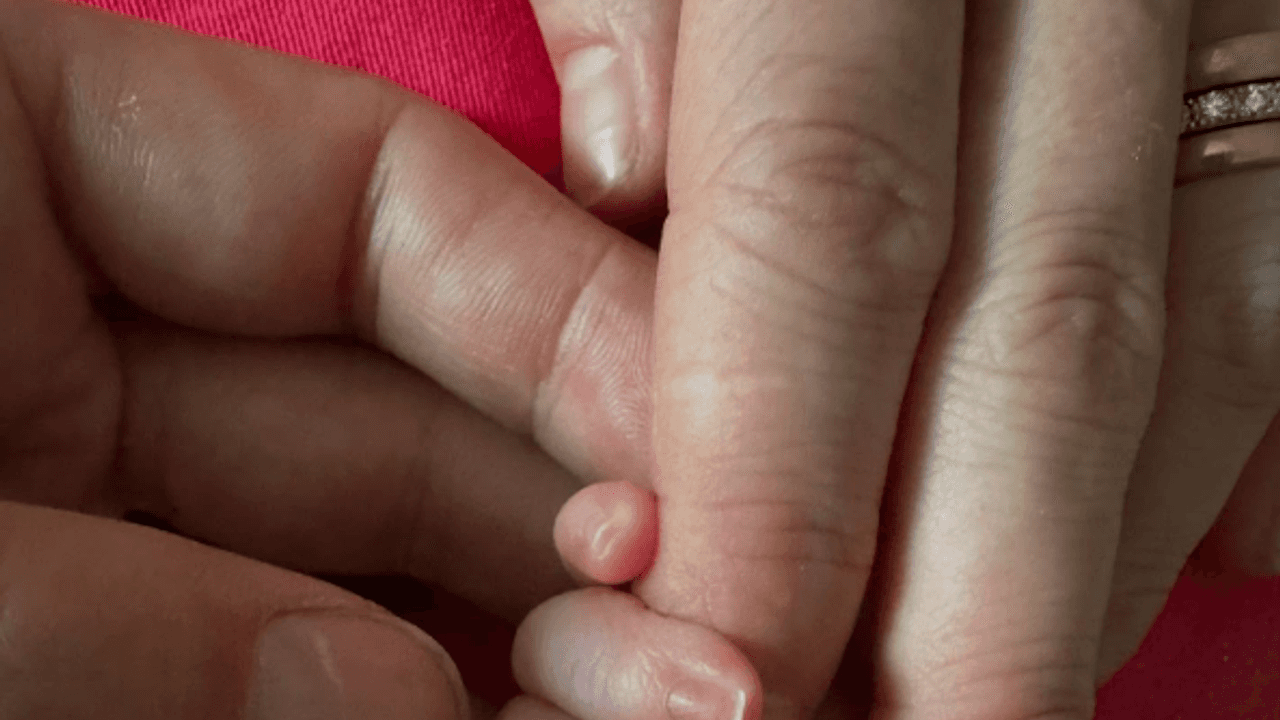 Eine Baby-Hand zwischen Fingern von Erwachsenen.