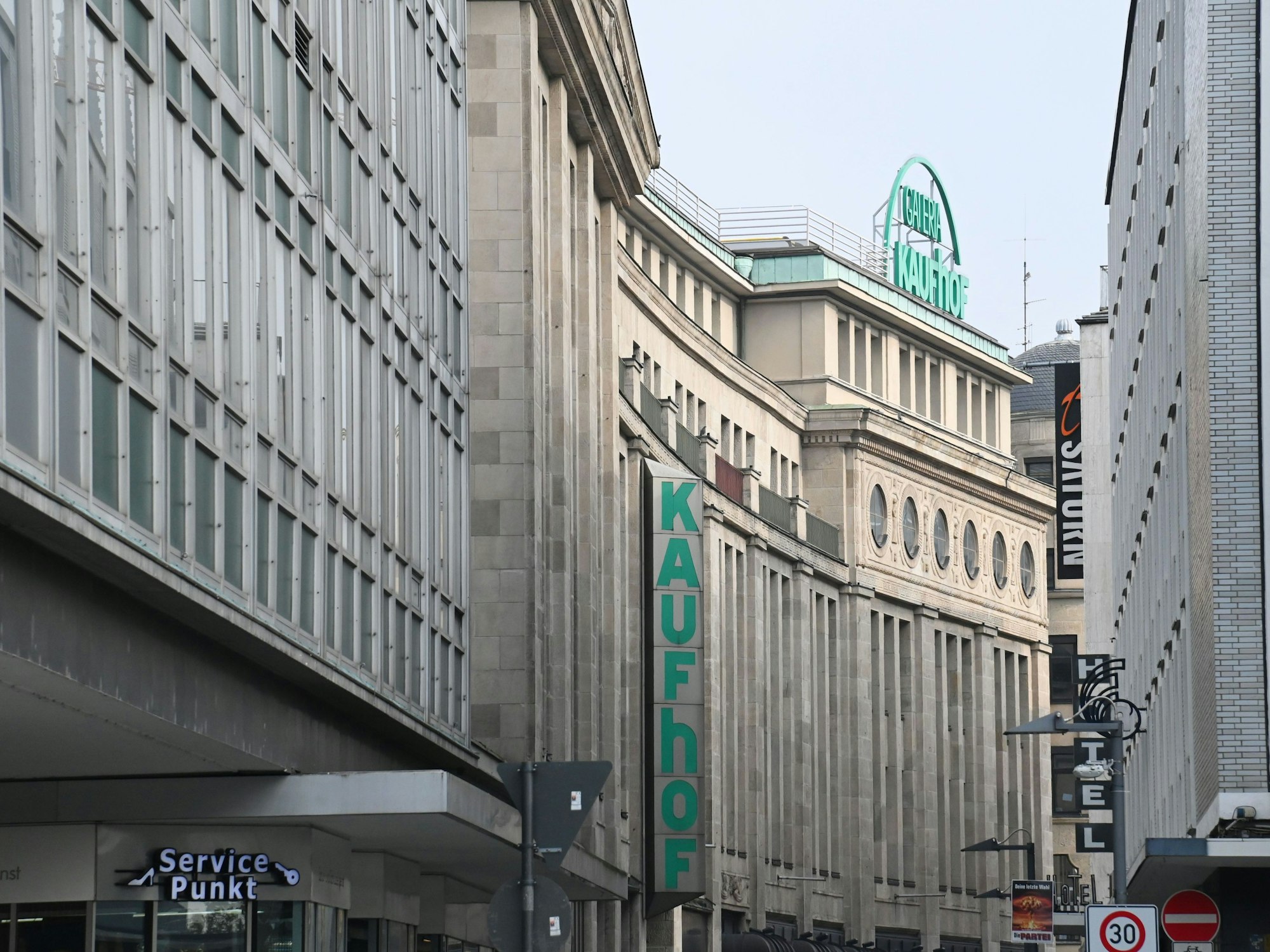 Eine Häuserreihen in der Kölner Innenstadt, an dem hinteren Gebäude hängen Schilder mit den Aufschriften Kaufhof und Galeria Kaufhof.