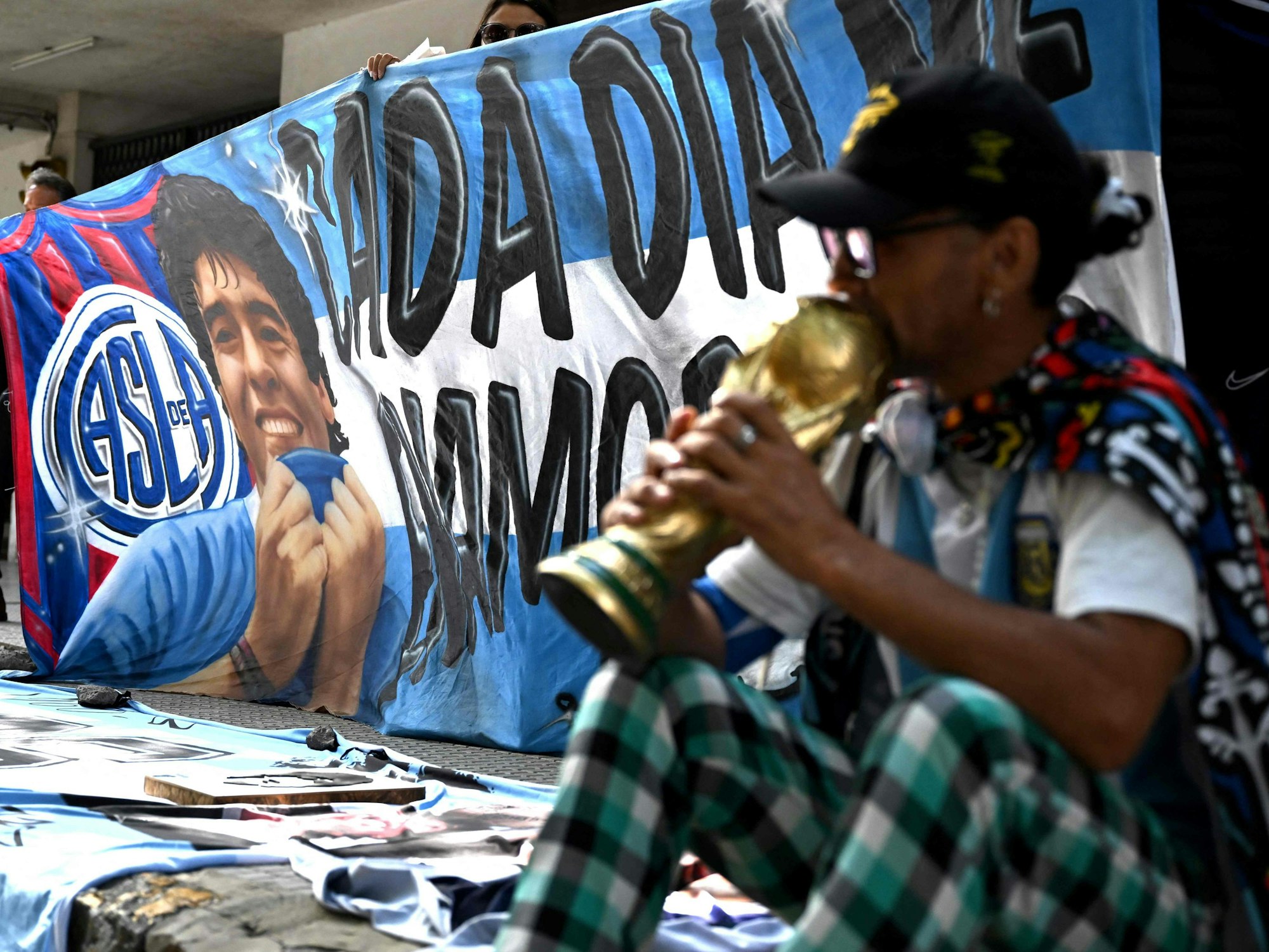 Ein Fan sitzt mit einem WM-Pokal vor dem Gericht.