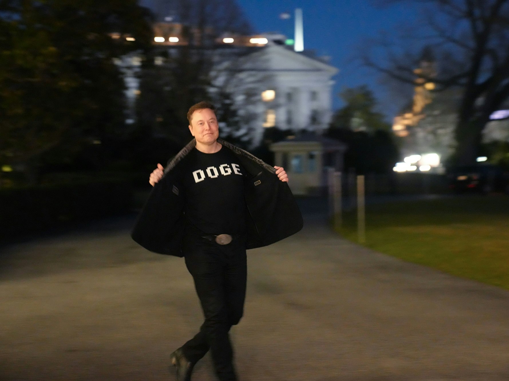 Elon Musk zeigt den Medien sein T-Shirt mit der Aufschrift „DOG“E, während er auf dem Südrasen des Weißen Hauses in Washington geht.