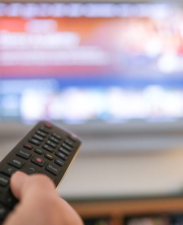 Zu sehen ist eine Hand die eine Fernbedienung für ein TV-Gerät bedient.