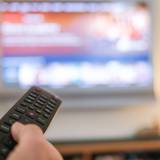 Zu sehen ist eine Hand die eine Fernbedienung für ein TV-Gerät bedient.