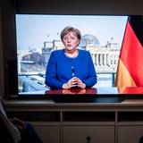 Menschen schauen die TV-Ansprache der Bundeskanzlerin Angela Merkel (CDU) 2020 in einem Wohnzimmer. Die Bundeskanzlerin redet über die Coronavirus-Pandemie.