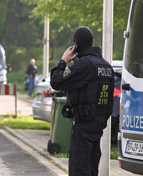 Ein Bundespolizist steht während einer Razzia auf der Straße und telefoniert.