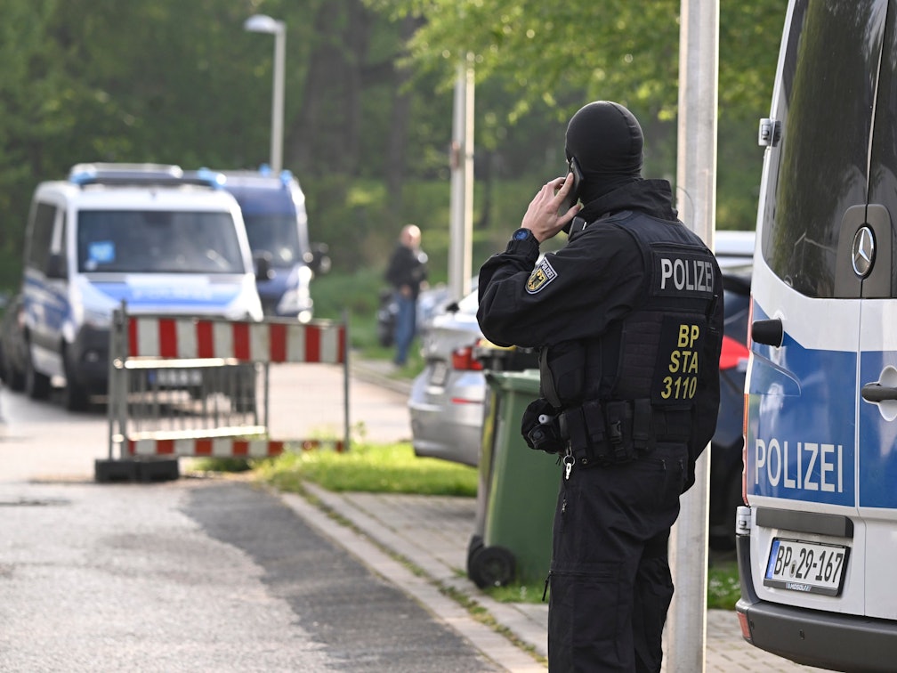 Ein Bundespolizist steht während einer Razzia auf der Straße und telefoniert.