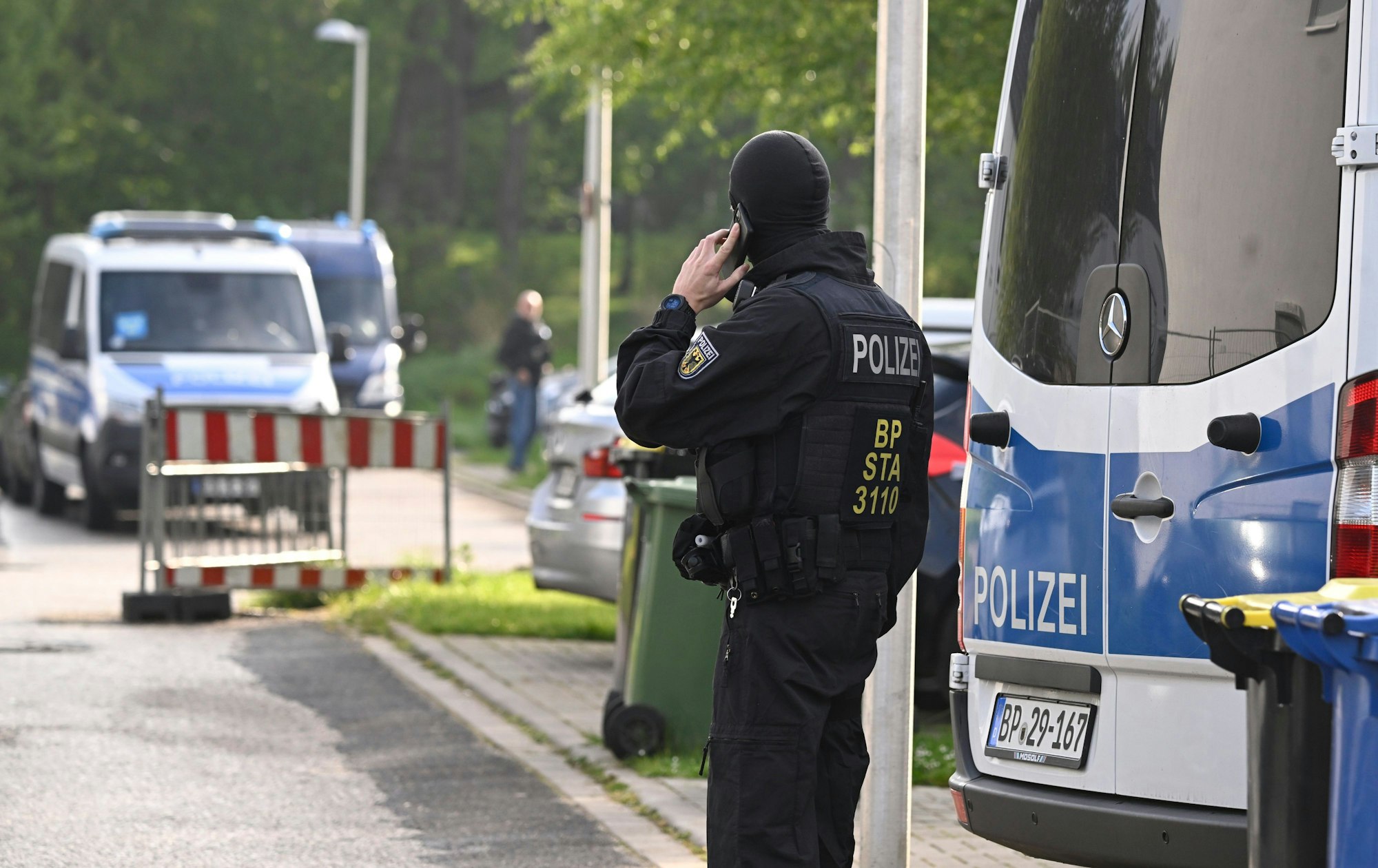 Ein Bundespolizist steht während einer Razzia auf der Straße und telefoniert.
