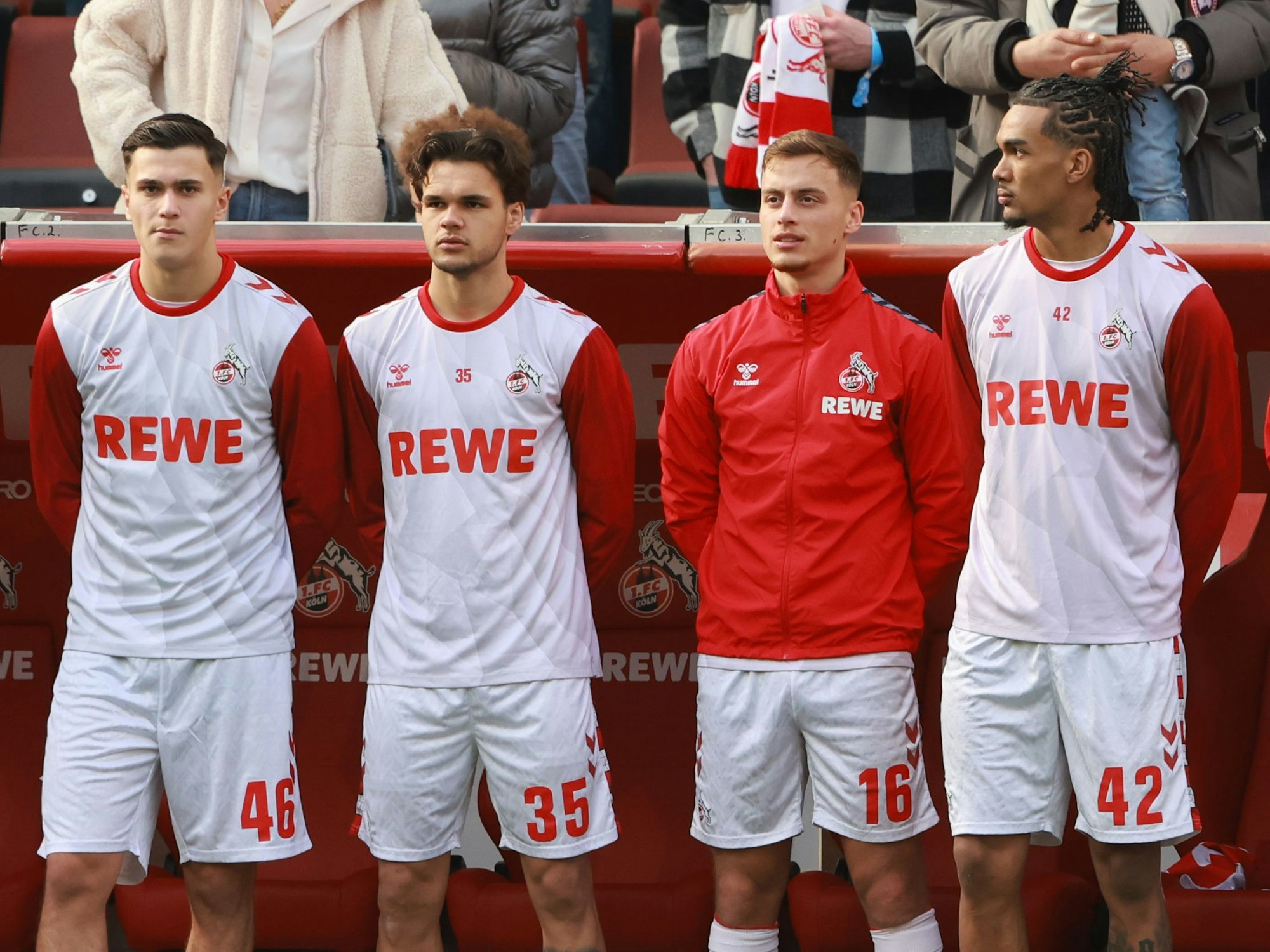 Die Spieler des 1. FC Köln stehen vor der Auswechselbank und halten ihre Hände verschränkt hinter den Rücken.
