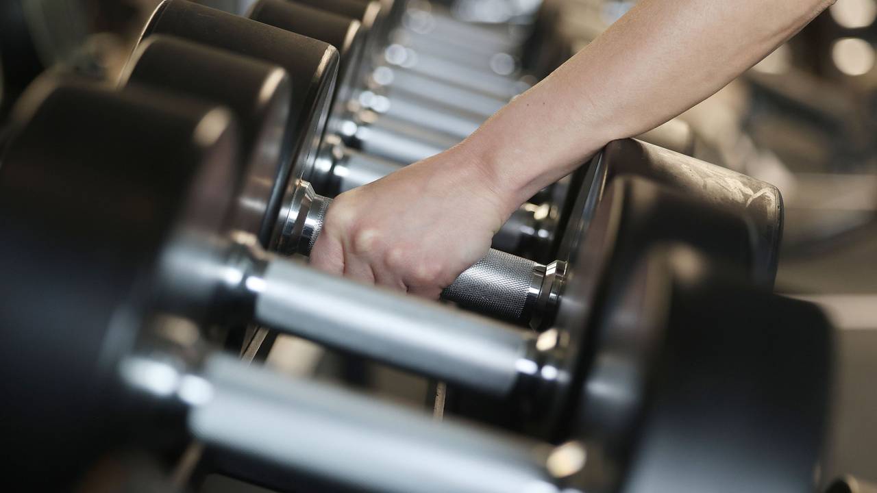 Eine Person greift Hanteln in einem Fitnessstudio.