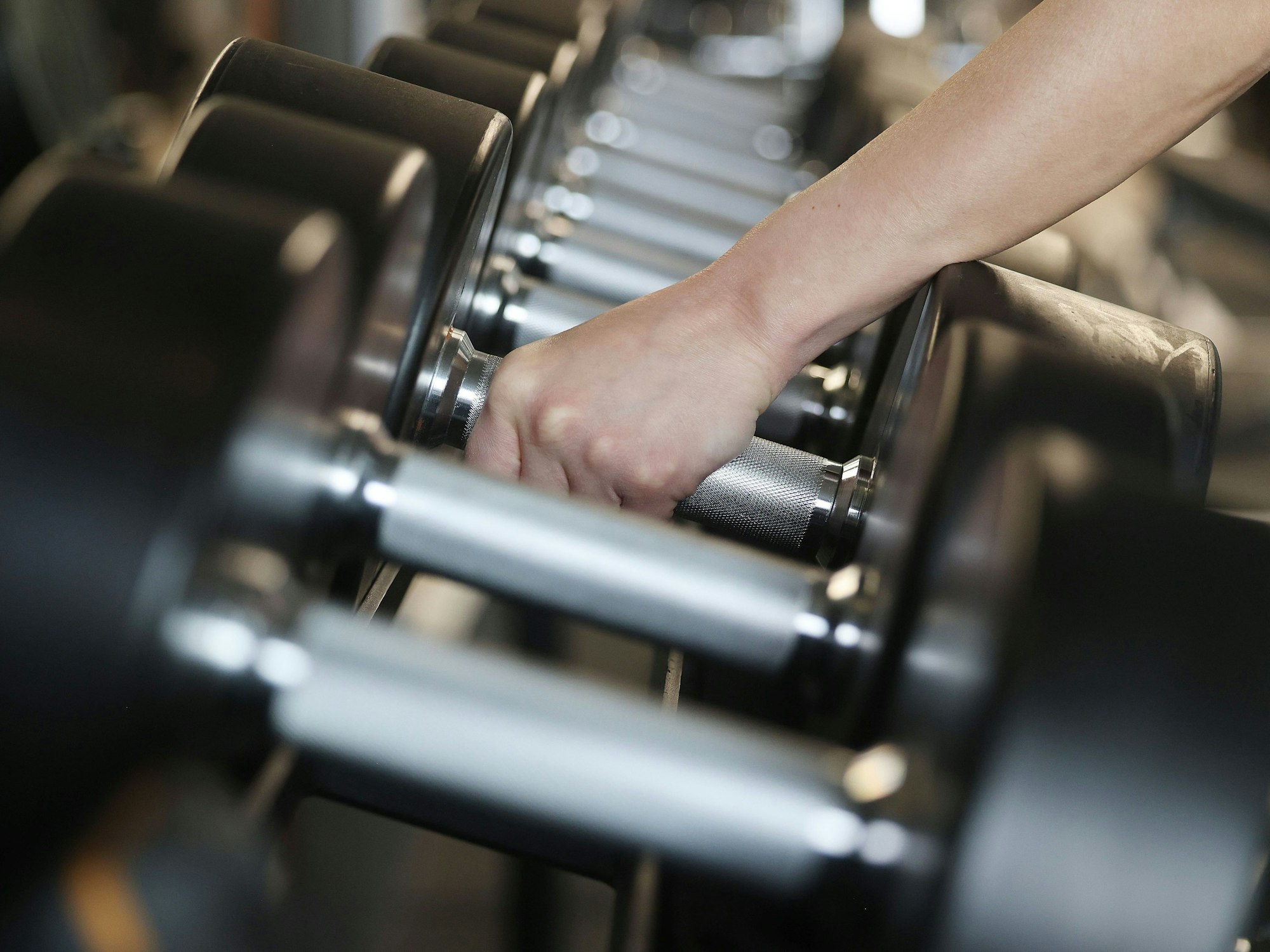 Eine Person greift Hanteln in einem Fitnessstudio.