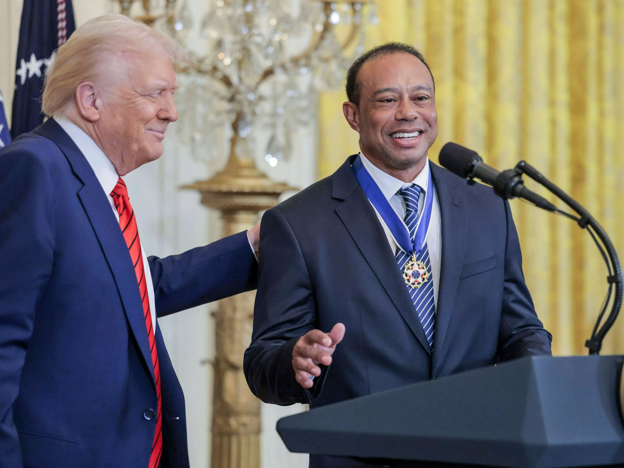 Donald Trump schlägt Tiger Woods auf den Rücken.