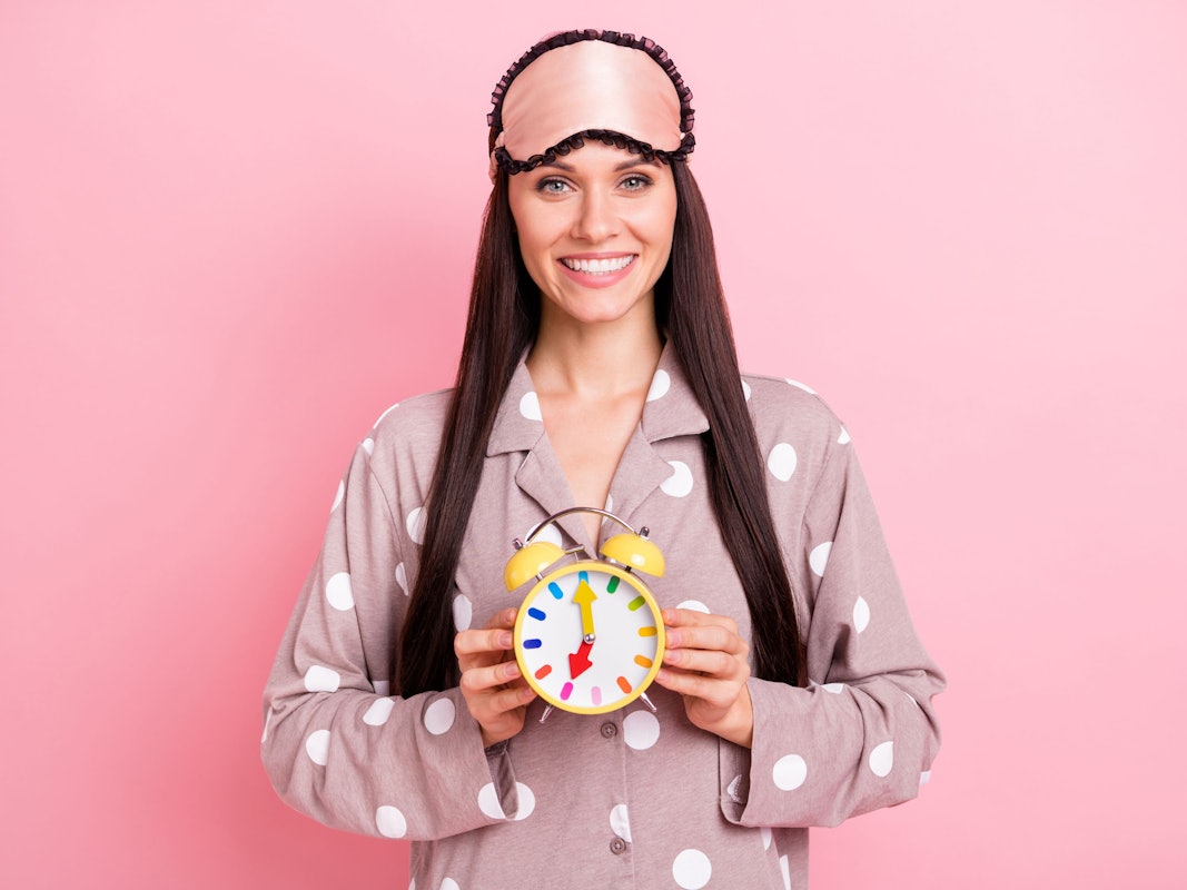 Frau hält Wecker mit Uhrzeit 7 Uhr in der Hand