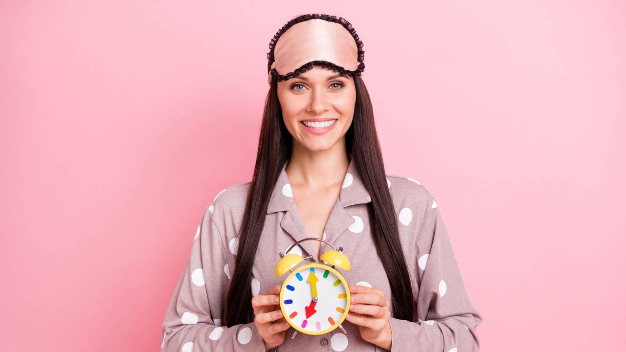 Frau hält Wecker mit Uhrzeit 7 Uhr in der Hand