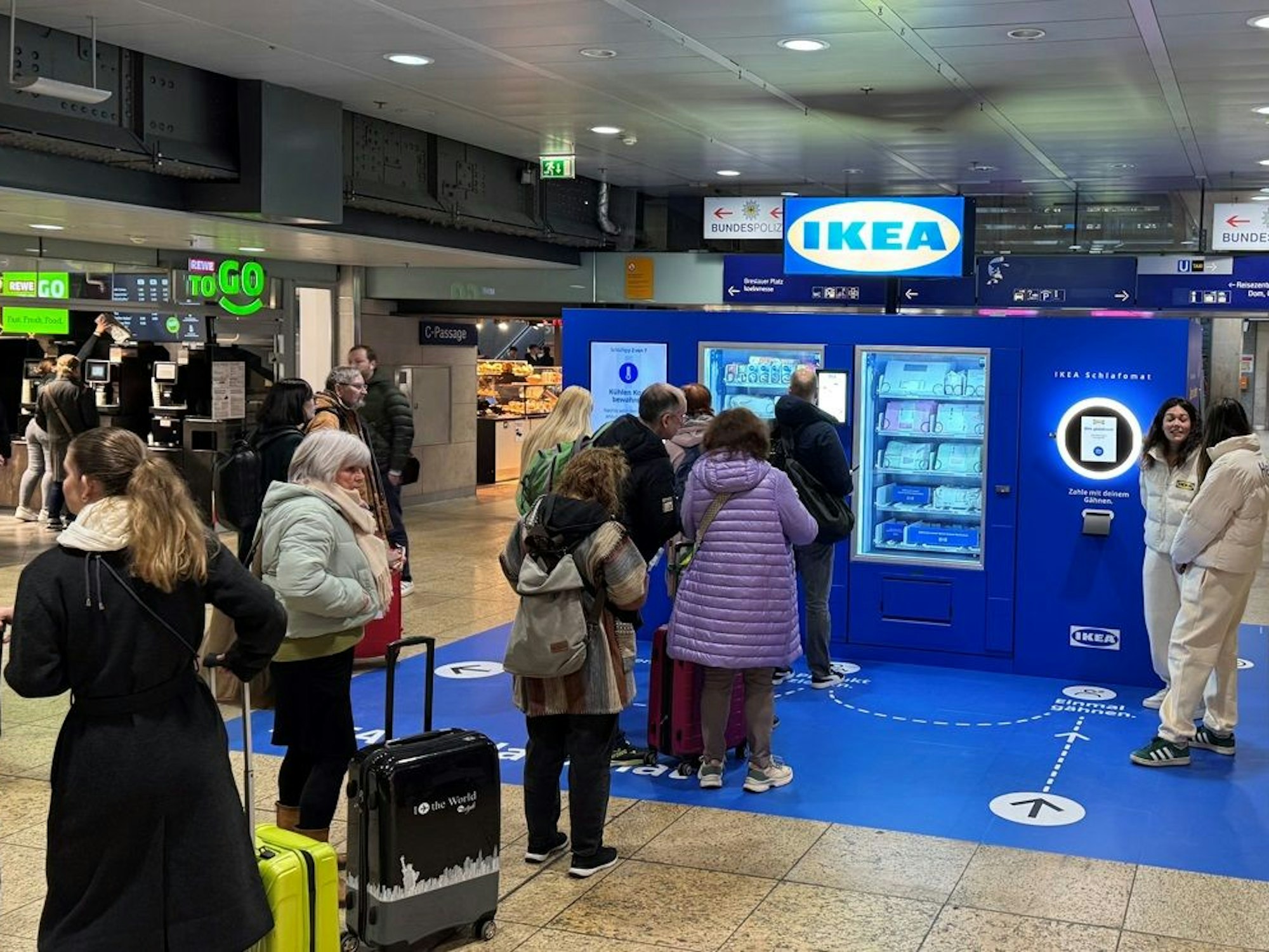 Vor einem Automaten von Ikea stehen mehrere Menschen Schlange.