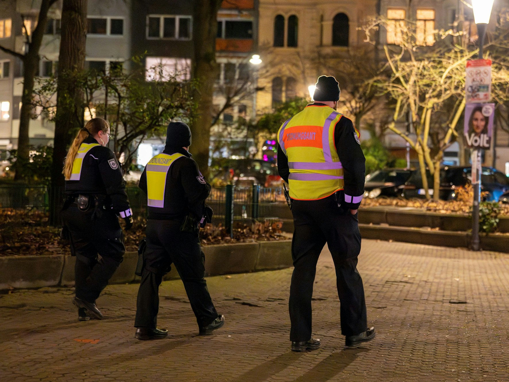 Drei Personen vom Ordnungsamt laufen über einen sonst menschenleeren Platz.