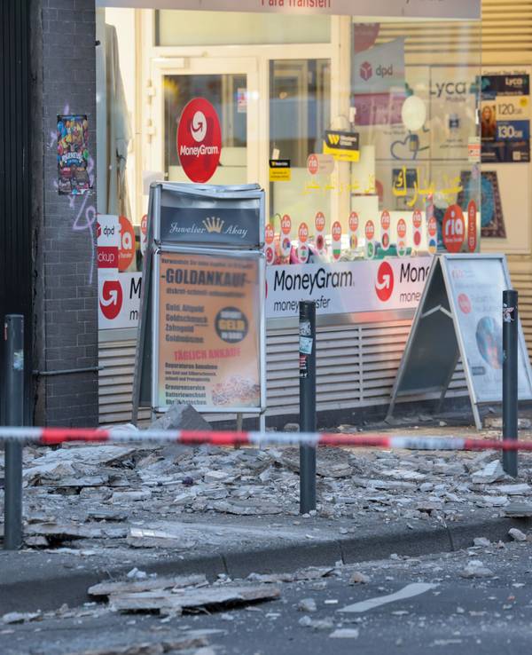 Trümmer, die sich von der Fassade eines Hauses gelöst haben, liegen auf einem Gehweg.