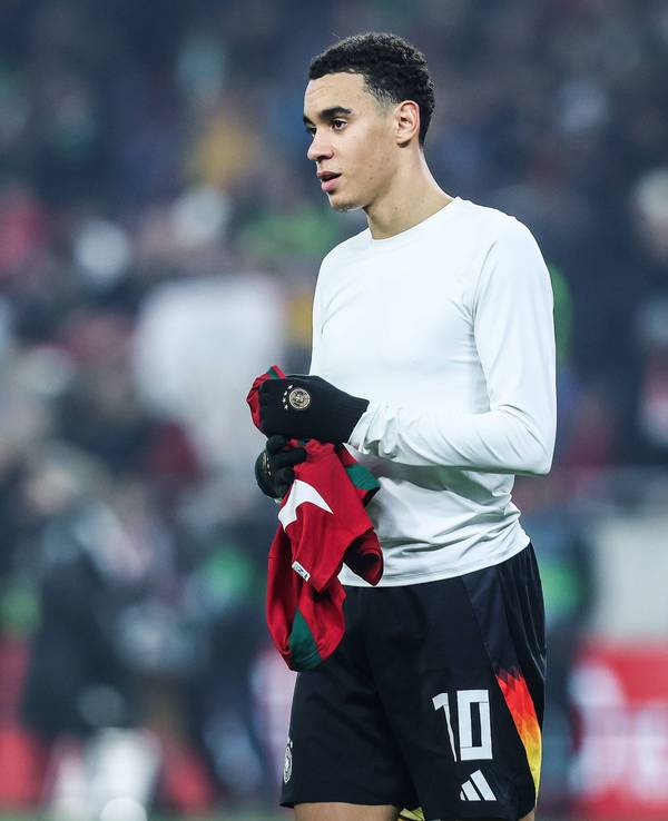 Jamal Musiala hält nach dem Trikottausch ein Shirt in den Händen.